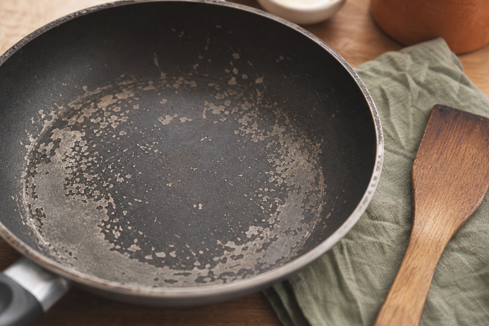 Close-up of a scratched, flaking nonstick coating on an old pan beside a wooden spatula